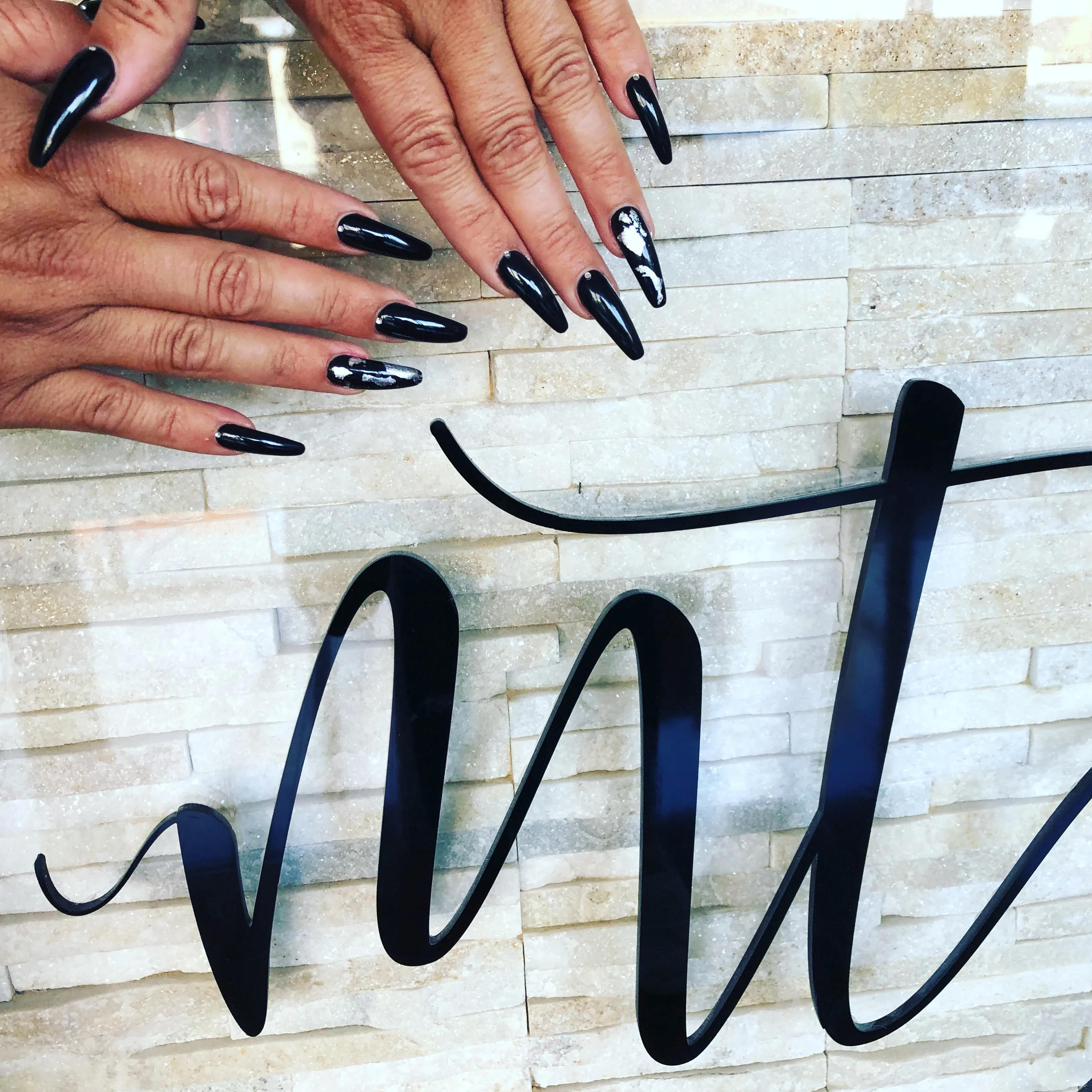 Glossy black stiletto nails against the salon's stacked-stone wall